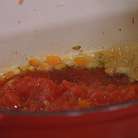Когда лук станет золотистым, добавить помидоры в собственном соку, томатную пасту и молотый перец чили, все перемешать и прогревать пару минут.