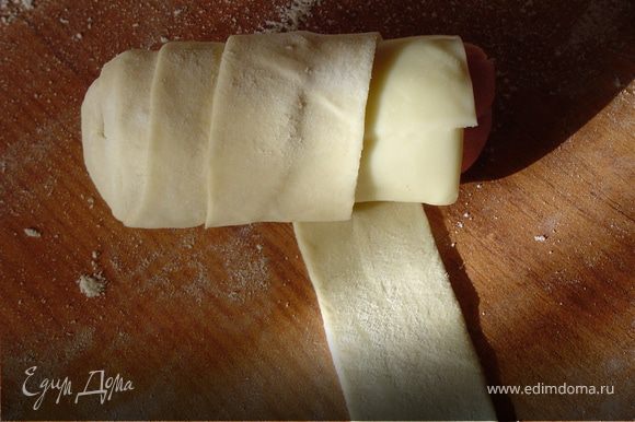 Полосками теста оберните брусочки ветчины с сыром так, чтобы очередной виток закрывал 1 /2 предыдущего.