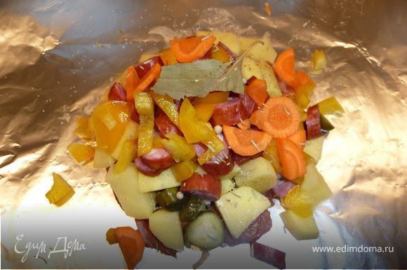 Собираем блюдо на 1 порцию: на лист фольги (примерно 30х30 см) в центр выкладываем слоями (немного солим и перчим каждый слой): мясо, чеснок (втыкаем в мясо), лук, корнишоны, сельдерей, картошку, колбаски, болгарский перец и морковь. В центр кладем часть лаврового листа, несколько горошин черного или белого перца, немного солим. Можно сверху в центр влить 1 ст.л. красного сухого вина ИЛИ острой томатной пасты.