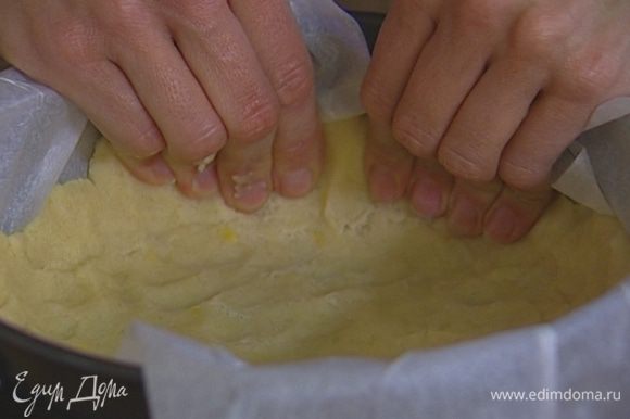 Разъемную форму для выпечки (20 см) выстелить пекарской бумагой, выложить 2/3 теста и равномерно его распределить, чтобы получились бортики до середины формы.