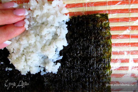 На лист раскладываем рис тонким слоем с небольшим усилием, так чтобы он прилипал к листу нори равномерно.