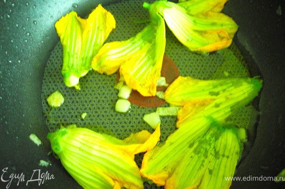 Нарезать чеснок, добавить его в нагретую сковороду с маслом, обжарить в течение нескольких секунд, выложить цветки тыквы (цуккини) на сковороду.