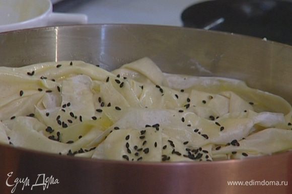 Пласты теста смазать оливковым маслом, уложить «морщинками» на начинку, проколоть вилкой и присыпать сверху кунжутным семенем.