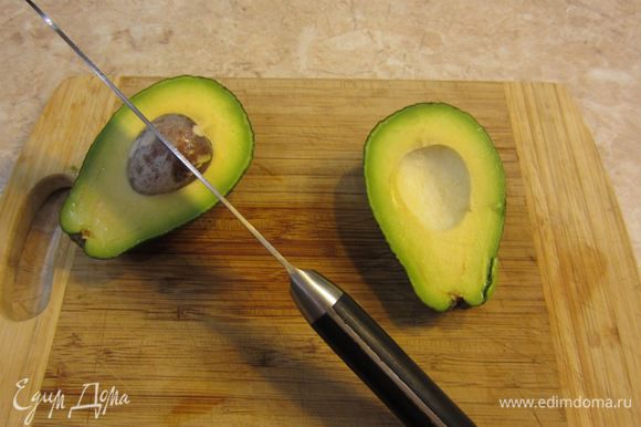 Прорежьте мякоть авокадо вокруг косточки. Покрутите одну половину авокадо по отношению к другой. Одна часть легко отделится от косточки. Осторожно ударьте лезвием по косточке. Лезвие воткнется. Поверните нож с косточкой и она отделится от мякоти.