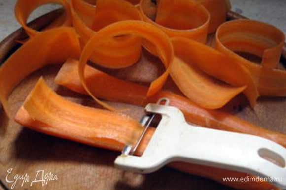 Готовый торт остудить, достать из формы и присыпать сахарной пудрой. Приготовить морковь для украшения торта. Для этого очистить крупную морковь и нарезать её с помощью ножа для чистки картофеля на тонкие-тонкие длинные ломтики.