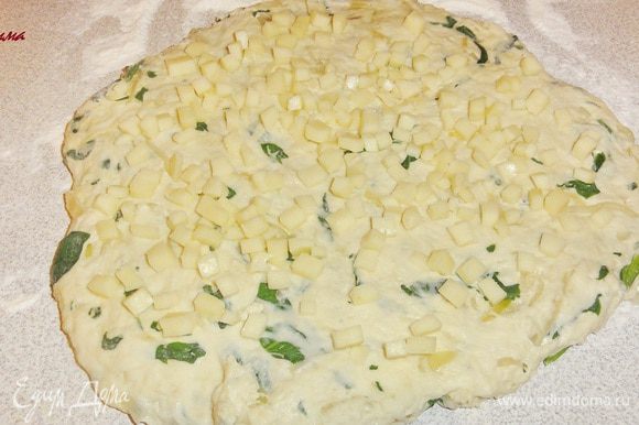Тесто увеличится 2-2,5 раза. Выложите тесто на стол посыпанный мукой и придайте тесту форму лепешки руками. Нарежьте сыр мелкими кубиками. Распределите сыр на поверхности теста.