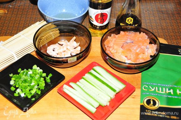 Подготовим все ингредиенты: 1) Рыбу нарезать тонкими брусочками 2) Креветки окунуть в кипящую подсоленную воду на 2-3 минуты, слить, остудить и почистить 3) Огурец порезать тонкими брусочками 4) Мелко нарезать зелёный лук (достаточно несколько пёрышков) 5) В отдельную мисочку налить рисовый уксус (можно немного разбавить холодной водой) для смачивания рук