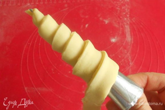 Дальше раскатывать и складывать тесто не рекомендуется, так как тонкие слои могут разорваться, вследствие чего масло перемешается с тестом и изделия получатся с маленьким количеством слоев. Готовое тесто раскатайте в прямоугольный пласт толщиной около 5–6 мм, нарежьте его на длинные полосы шириной 1,5–2 см. Возьмите в правую руку конусную жестяную или бумажную трубочку, а в левую — конец полосы теста, прикрепите его к узкому концу трубочки. Поворачивая правой рукой трубочку, расположите полоску по спирали, следя за тем, чтобы один край теста находил на другой. Заворачивать полоску теста надо по направлению от узкой части конуса к широкой, при этом лента растянется до толщины 3–4 мм. Всего надо сделать 5–6 витков.