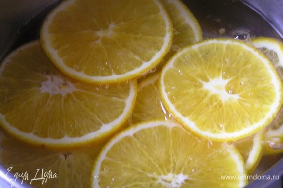 Приготовить декор-начинку. Вскипятить воду, добавить сахар и перемешать до растворения, добавить нарезанные тонкими ломтиками апельсины, варить 10-12 минут.
