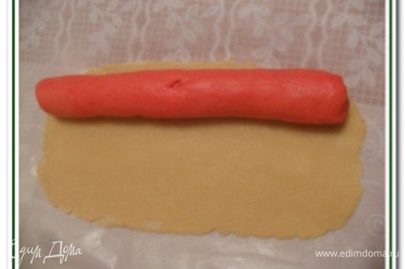Из красного теста сформировать колбаской длинной 22 см и положить на белое раскатанное тесто с краю и завернуть рулетом с помощью пергаментной бумаги.