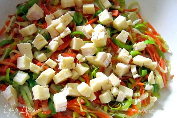 Сыр нарезать небольшими кубиками. Половину сыра добавить в сотейник к овощам. Посолить, поперчить по вкусу и перемешать.