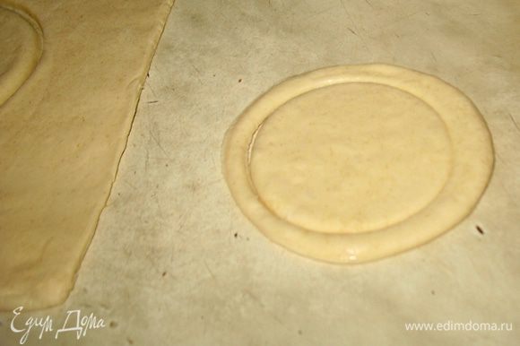 Раскатываем тесто толщиной 0,5 см. Из теста вырезаем 8-мь кругов диаметром 10 см, в 4-х из них вырезаем меньшего диаметра круги, не вынимаем, оставляем на месте. Целые круги по краю смазываем водой и сверху выкладываем круги с вырезанными кругами. Слойки смазываем взбитым желтком. Слойки выкладываем на застеленный пергаментом противень и ставим в предварительно разогретую до 190 градусов духовку минут на 10. Дальше снижаем температуру до 170 градусов и выпекаем слойки еще минут 15 до золотистой корочки. Вынимаем слойки даем немного остыть и вынимаем вырезанные круги, т.е. крышечки.