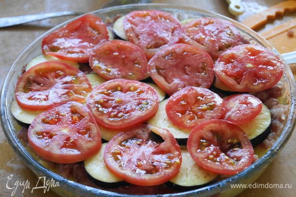Затем выложить обжаренные баклажаны, после чего помидоры. Чуть-чуть посолить, на помидорки положить мелко нарезанный чеснок.