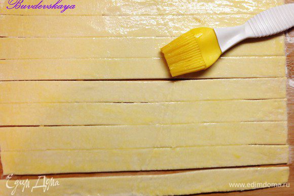 Раскатать тесто на присыпанной мукой поверхности и разрезать на полоски шириной 2,5- 3 см. Смазать полоски взбитым яйцом.