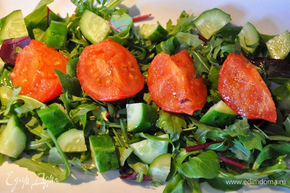 На тарелку выложить зелень, затем порезанный крупными кубиками огурец. Выложить помидоры и все посолить.