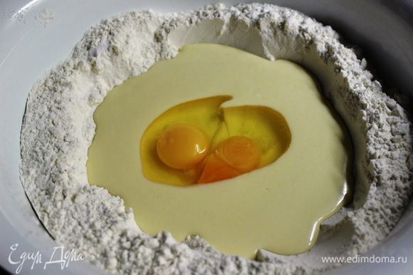 В большое блюдо просеять муку (3/4 части) и добавить разрыхлитель. В центре сделать углубление, вылить в него масляную смесь и разбить два яйца.