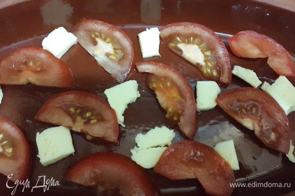 В глиняную тарелку равномерно выложить сливочное масло кусочками и помидоры.