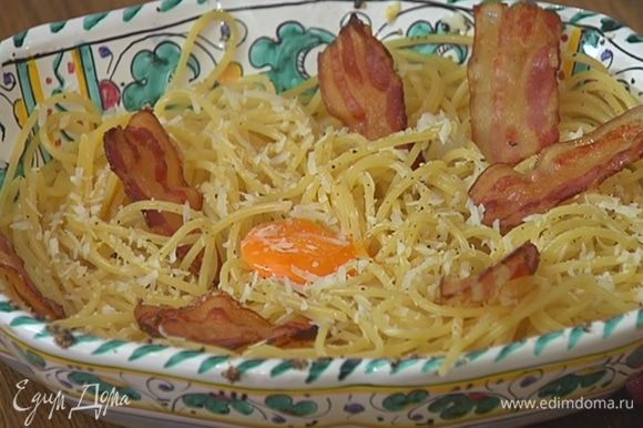 Спагетти еще немного поперчить, выложить на макароны сверху желтки пашот, посыпать оставшимся сыром и украсить чипсами из бекона.