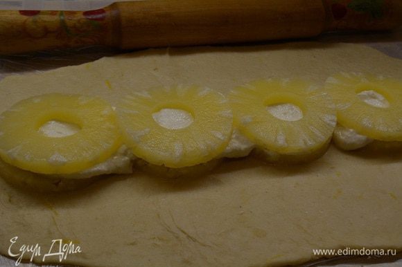 На ананасы выложить творожную начинку и снова ряд ананасов. Взяв за края пищевой пленки, поднять тесто с двух сторон к середине. Тем самым соединить два края тесто, чтобы получился прямоугольник.