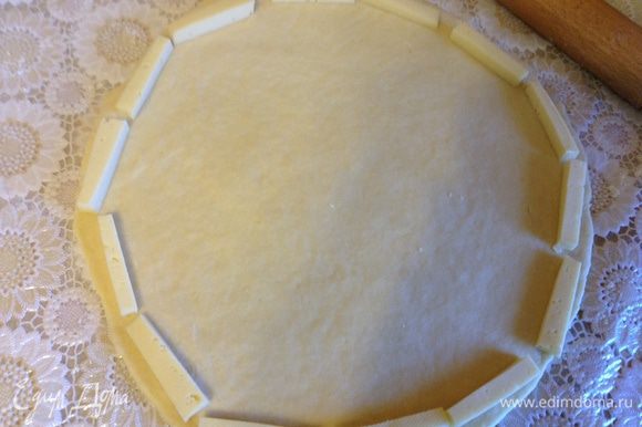 Раскатать тесто в круг, по краю выложить остаток сыра нарезанный брусочками.