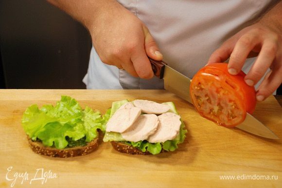 На сэндвич выложить листья салата, нарезанный огурец, куриное филе, а затем ломтики помидора.