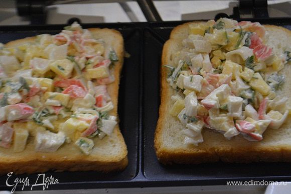Сэндвичницу разогреть. Уложить хлеб для тостов. Выложить начинку, — не жалеем. И накрыть верхним куском хлеба.