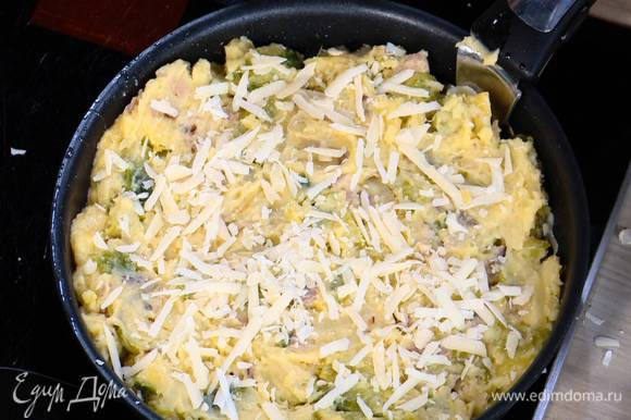 Дно сковороды, где жарился лук с грудинкой, посыпать половиной натертого сыра, выложить картофельно-капустную массу, разровнять ее и посыпать оставшимся сыром.