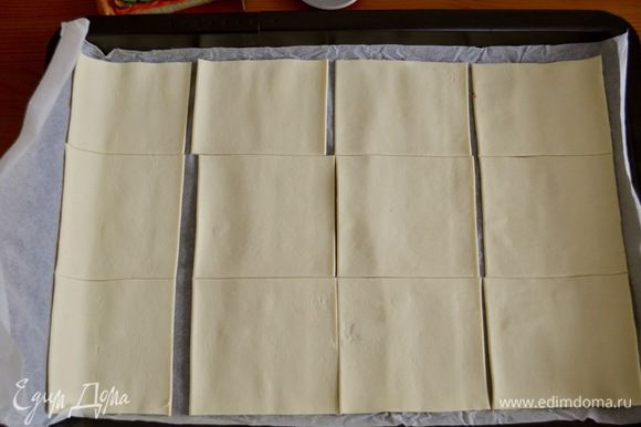 Готовое слоеное тесто развернуть и выложить на противень вместе с пекарской бумагой. Разрезать на квадраты со стороной 10 см.