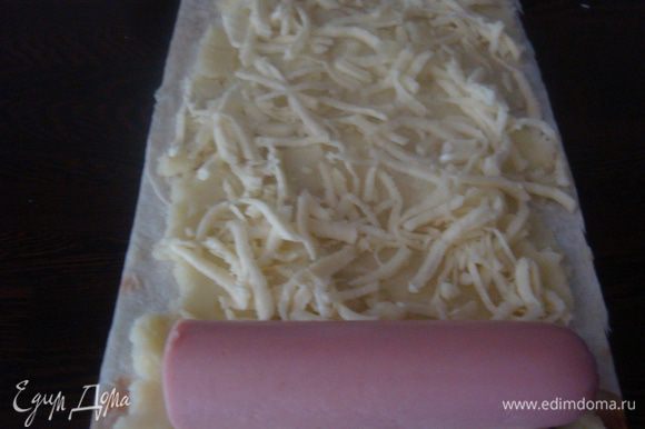 Берем лист лаваша, намазываем картофельным пюре, посыпаем сыром. На край листа лаваша кладем сосиску и заварачиваем в плотный рулет.