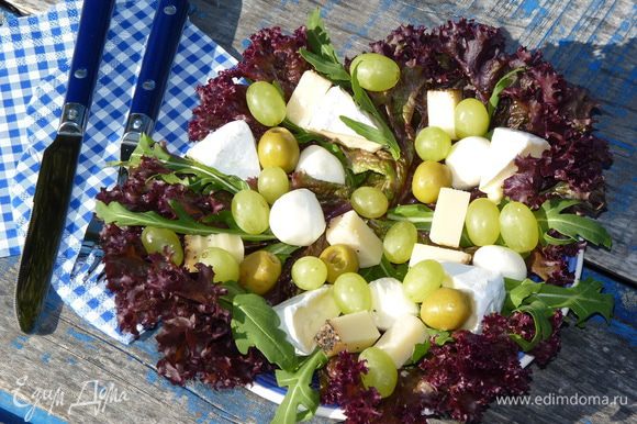 Листья салата выложить на тарелки, добавить руколу. Сыр нарезать брусками, бри — дольками. Выложить сверху салата, добавить моцареллу, виноград, орехи и оливки.