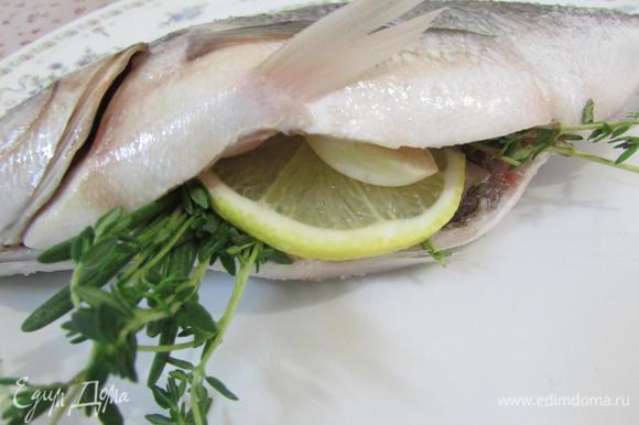 В брюшко каждой рыбы положить травки, по пластинке чеснока и лимона.