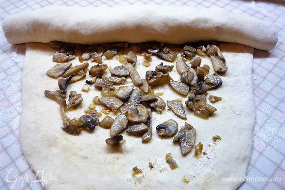 Раскатываем тесто в пласт, распределяем начинку из грибов, оставляя свободные края примерно 4 см и сворачиваем в толстый рулет.