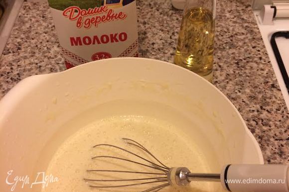 Молоко «Домик в деревне» довести до кипения и влить тонкой струйкой в тесто, непрерывно взбивая венчиком. Затем добавить растительное масло и еще раз хорошо взбить.