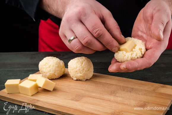 Из рисовой массы влажными руками сформировать шарики, поместив внутрь каждого квадратик мягкого сыра.