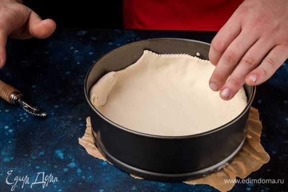 Выложите в форму слоеное тесто, наколите вилкой в нескольких местах. Бортики необходимо оставить высокими, чтобы начинка не вытекла. Разогрейте духовку до 180°С.