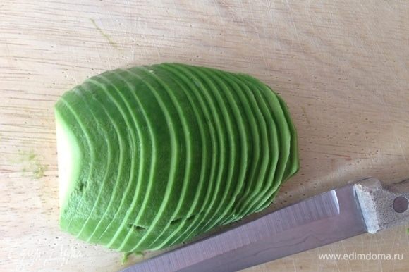 Авокадо разрезать на 2 половинки, удалить косточку и очистить от кожицы. При помощи тонкого ножа нарезать очень тонкими ломтиками.