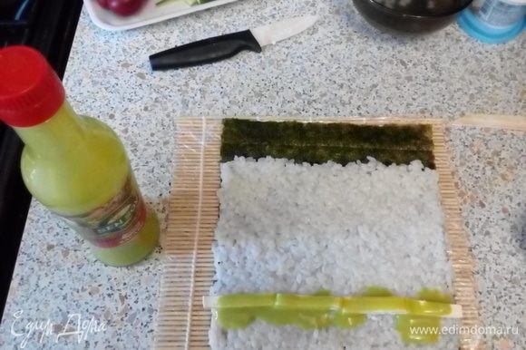 Выложить на шершавую поверхность нори рис, оставив 1–2 см листа не покрытым. Выложить бруски феты, полить соусом васаби.
