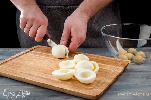 Куриные яйца отварите, охладите, очистите и разрежьте их вдоль пополам. Затем аккуратно выньте желтки и положите в миску. Белки накройте пищевой пленкой и поставьте в холодильник.