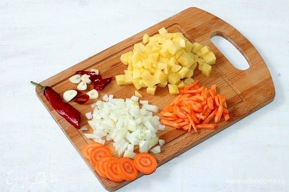 Подготовим овощи. Очищаем и нарезаем: картофель и лук — кубиками, морковь — соломкой, чеснок — слайсами, острый перец и сельдерей — дольками. Картофель отвариваем в оставшейся воде.