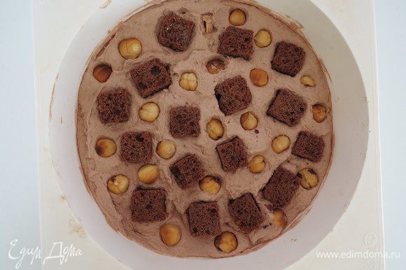 Равномерно распределить кубики шоколадного бисквита и обжаренный фундук, вдавливая их в ганаш, заморозить в морозилке до твердого состояния для удобства сборки.
