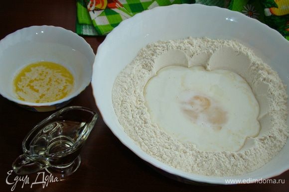 В муке сделать лунку, влить молоко, добавить яйцо, растительное масло и растопленное остывшее сливочное масло.