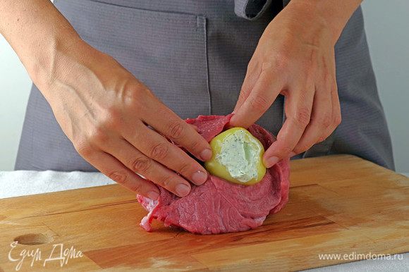 Разрежьте мясо вдоль почти до конца, слегка отбейте, положите в середину фаршированные перцы, оберните их говядиной, при необходимости замотайте рулет прочной ниткой.