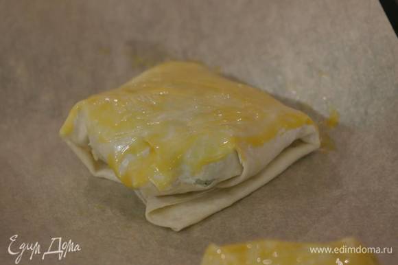 Поместить пирожки на противень, выстеленный бумагой для выпечки, смазать их желтком и выпекать в разогретой духовке 15 минут.