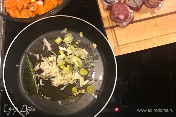 В форму для запекания выкладываем нарезанную колечками морковь. На сковороде с оливковым маслом и веточкой розмарина обжариваем давленый чеснок, нарезанный полукольцами лук-порей. Выкладываем на морковь.
