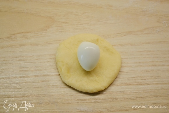 Тесто разделить на равные небольшие кусочки. Из каждого кусочка сформировать шарик, раскатать, на середину положить отварное очищенное перепелиное яйцо.