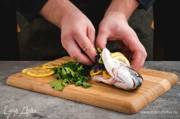 Сделайте несколько диагональных разрезов по бокам рыбы, вложите в них кружочки нарезанного лимона. Также нафаршируйте дораду лимоном и зеленью.