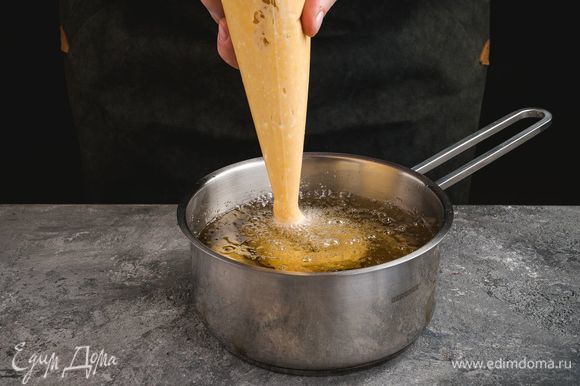 Тесто переложите в кондитерский мешок. Выдавливайте в горячее масло тесто произвольной формы. Обжарьте пончики в кипящем масле до золотистого цвета.