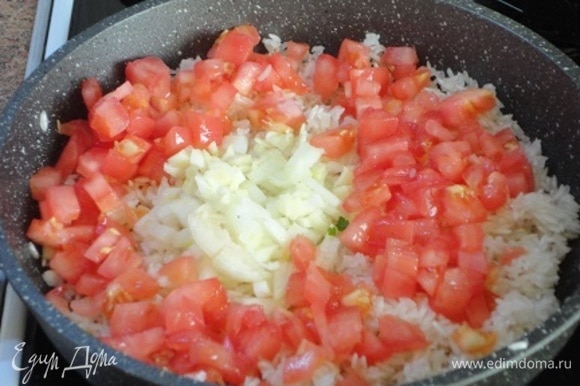К рису добавить лук с чесноком и помидоры, перемешать и тушить 3–4 минуты.