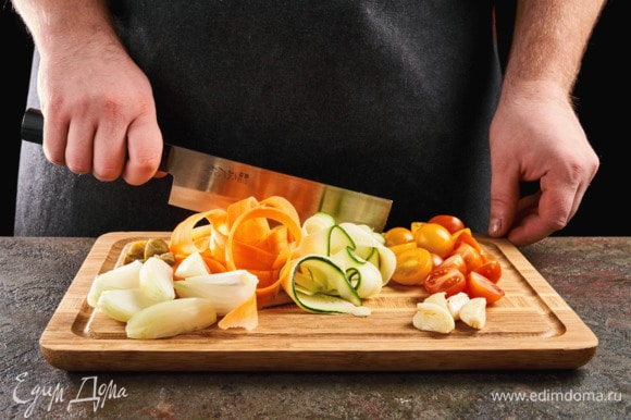 Нарежьте морковь и цукини слайсами, черри и каперсы — пополам, чеснок раздавите, лук крупно нарежьте.