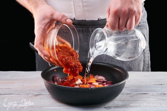 Выложите к луку и моркови томатную пасту, влейте 50 мл воды.